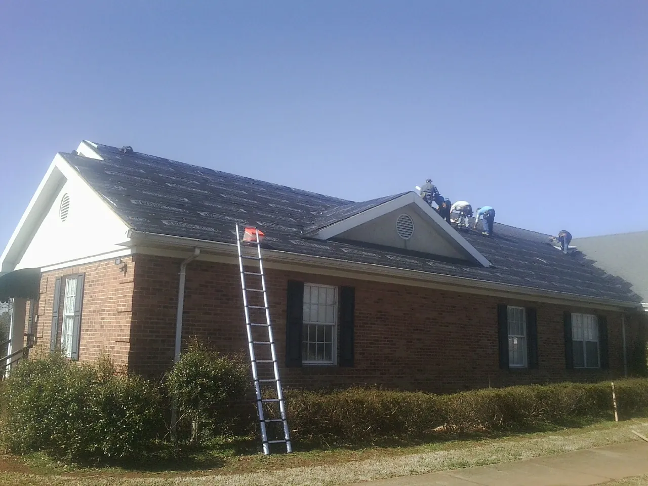 Crew tearing shingles off a brick ranch roof with a ladder set — Emergency Roof Repair work by our crew in Saint Donatus