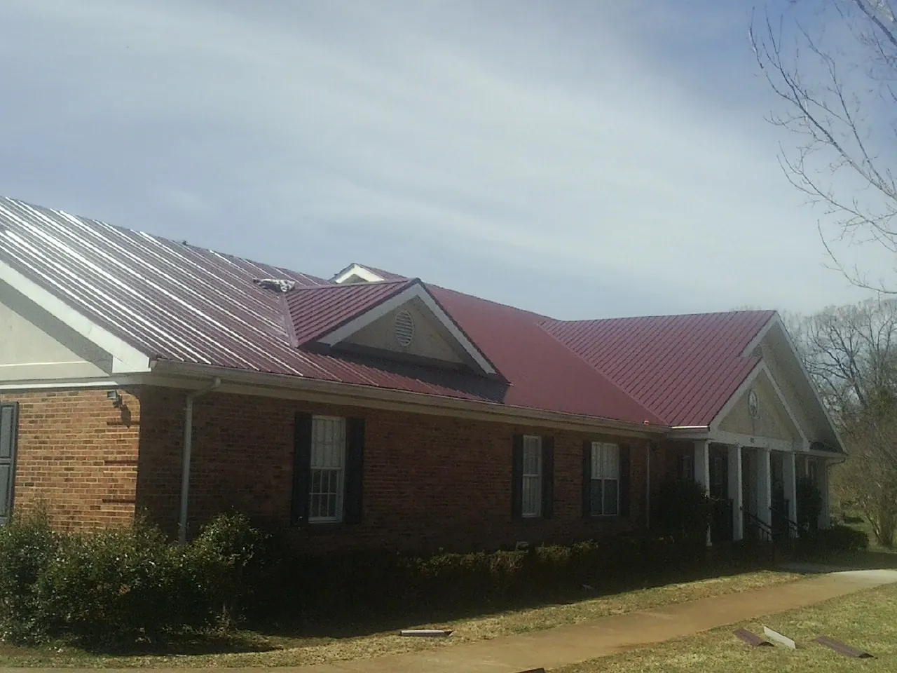 Red metal roof with gabled entries on a long brick building, from a Hail Damage Roof Repair job in Saint Donatus