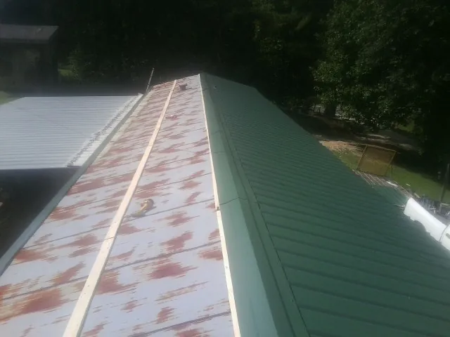 Old rusted panels beside newly installed green metal roofing — Wind Damage Roof Repair by Roofing Brothers in Saint Donatus