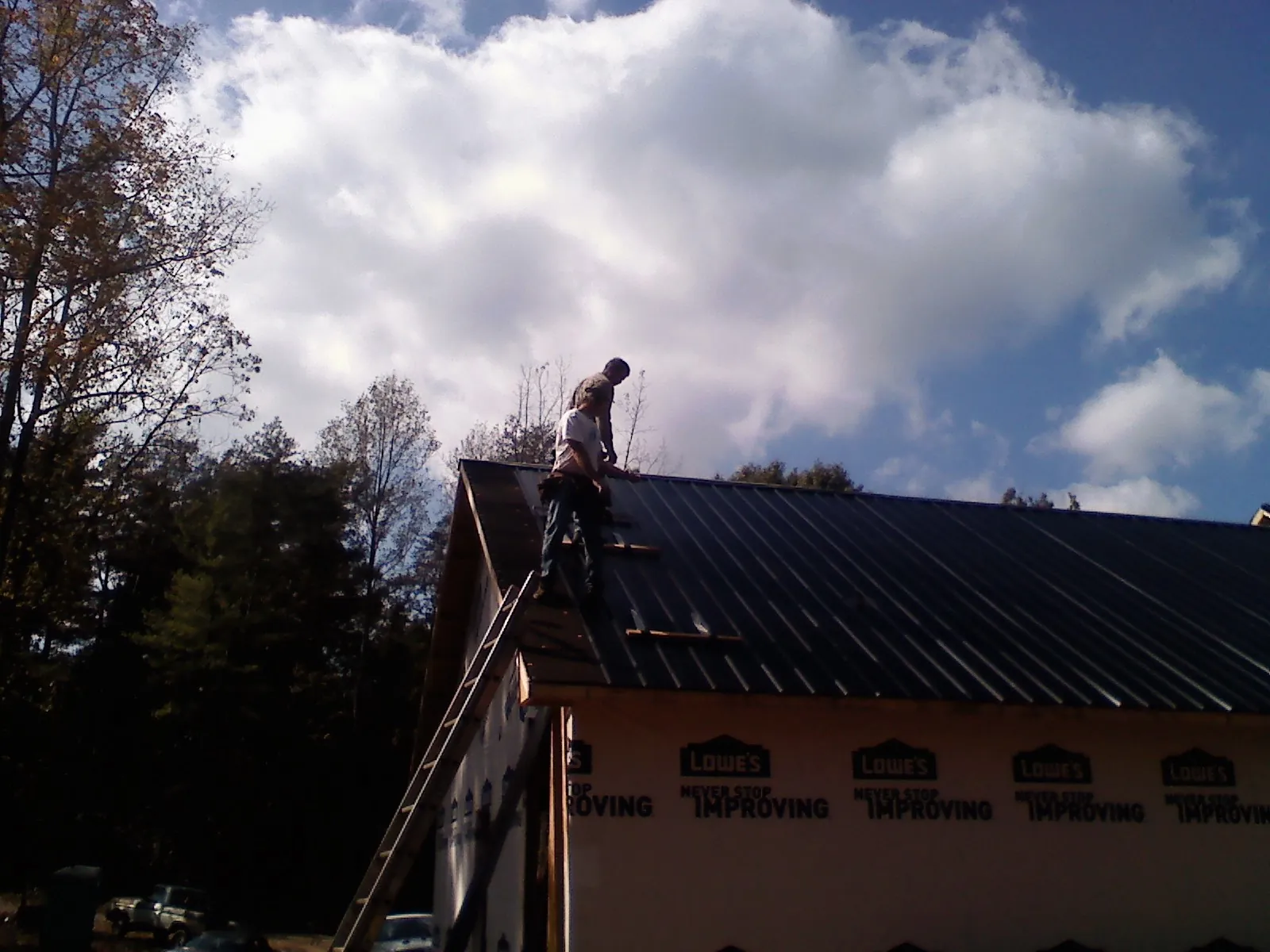 Roofer fastening dark metal panels high against a cloudy sky, from a Roof Inspection job in Saint Donatus
