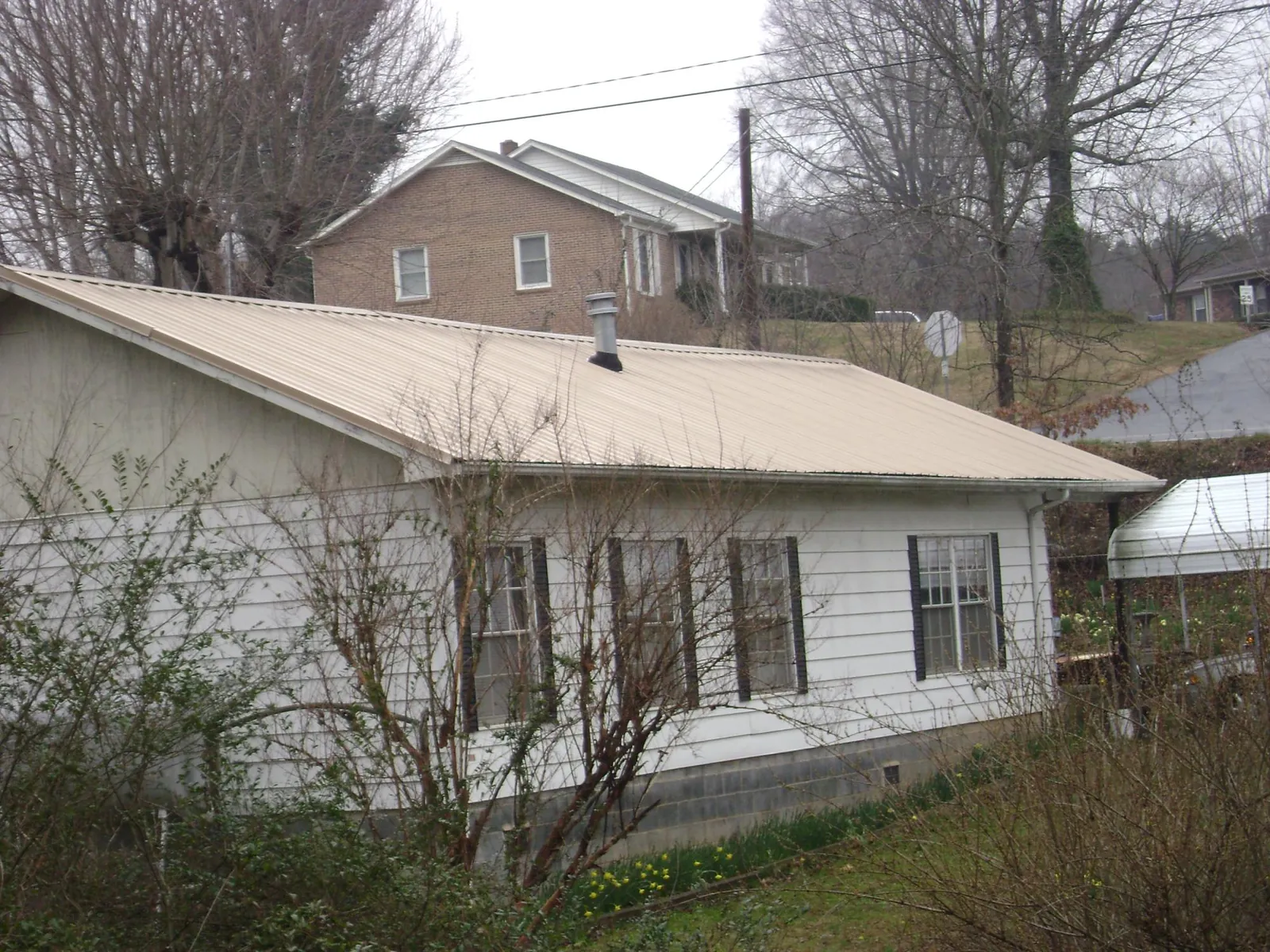 Tan metal roof on a white sided house set into a hillside — Commercial Roofing by Roofing Brothers in Saint Donatus