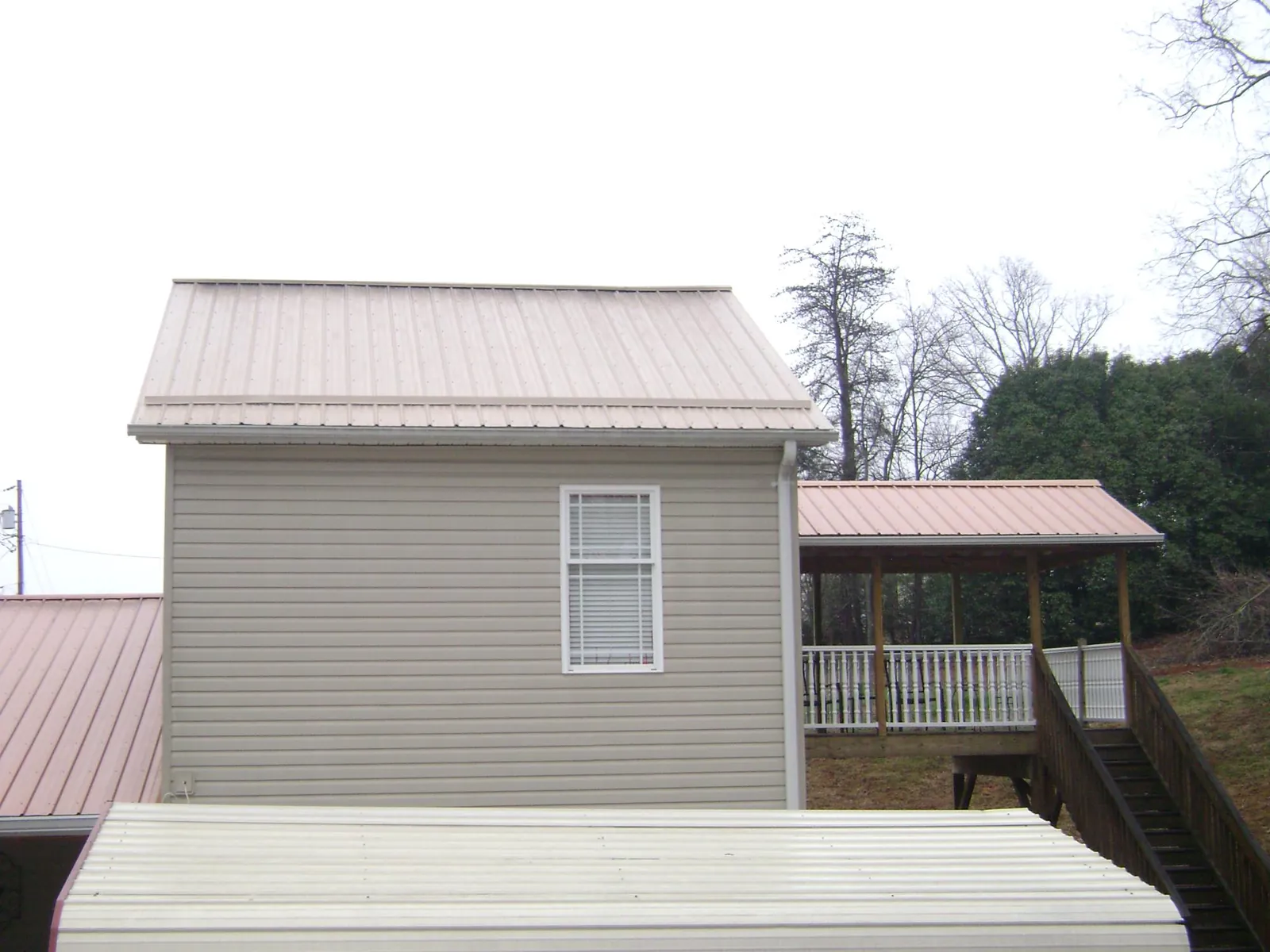 Tan metal roofs on a two story addition and attached porch, from a Roof Replacement job in Saint Donatus